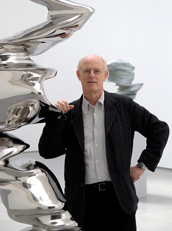 Abbildung zu: Tony Cragg vor einer anderen Arbeit aus Edelstahl. © VG Bild-Kunst, Bonn 2025