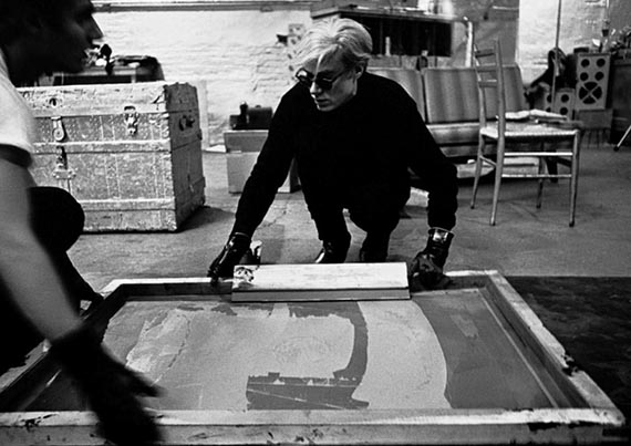 Abbildung zu: Andy Warhol bei der Arbeit an einer Serigrafie der "Campbell Soup I" in der Factory, New York, 1964. © Ugo Mulas Heirs. All rights reserved. / 2025 The Andy Warhol Foundation for the Visual Arts